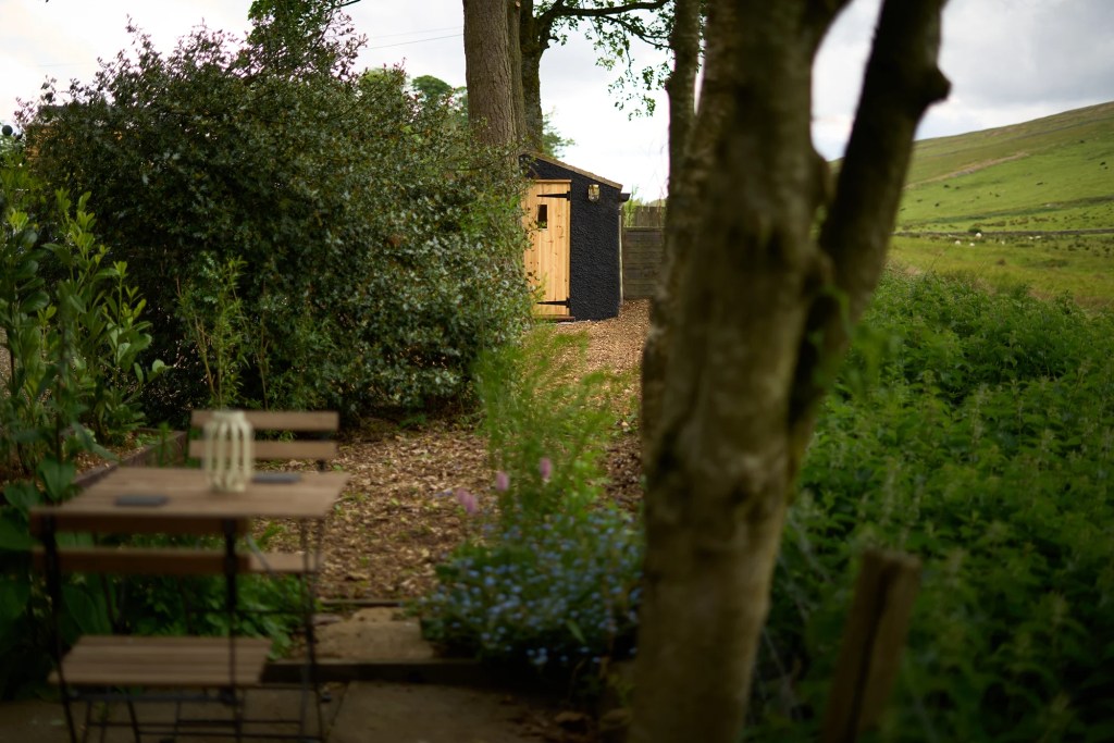 Hadrian's wall Hut's Sauna Shown through the trees with a dining bistro set in the foreground in Northumberland